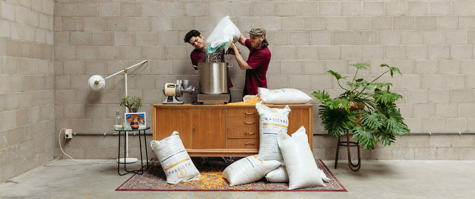 The two MasMais founders pouring a bag of corn into a steel nixtamal pot
