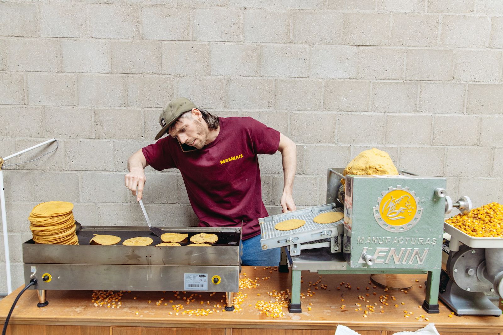 A MasMais founder flipping tortillas on the griddle beside the tortilla machine