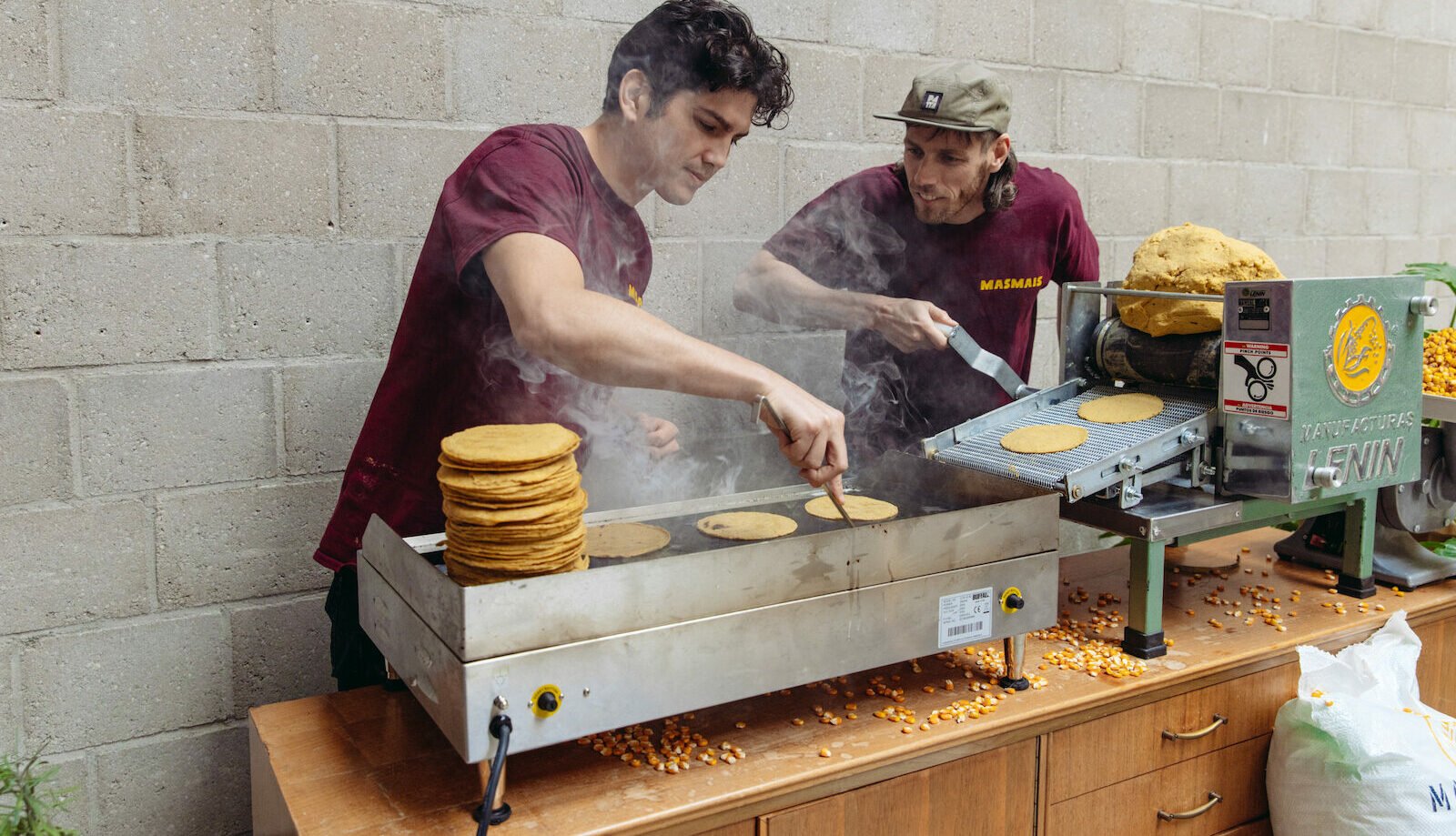 The two founders cooking fresh tortillas on the griddle beside the tortilla machine