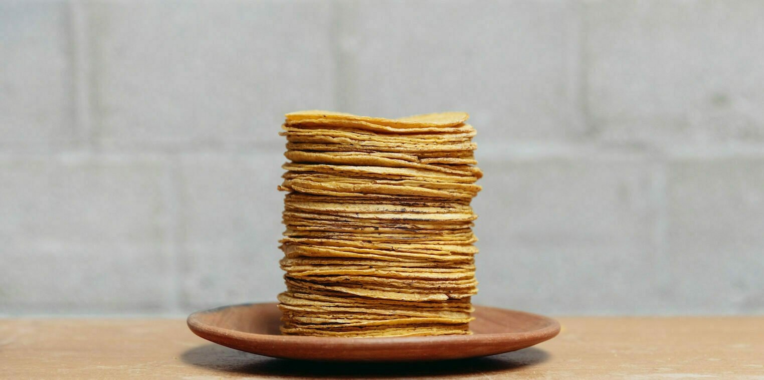 A tall stack of fresh corn tortillas on a clay plate