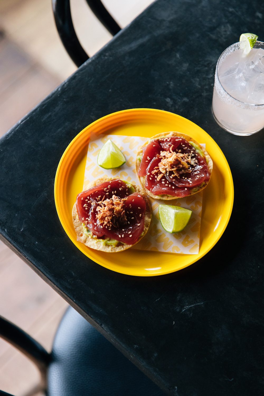 Two tuna tostadas with sesame and crispy shallots on a yellow MasMais plate, margarita beside